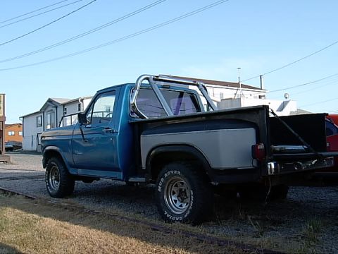 1983 Ford F-150 - This blue pickup truck, likely from the early 1980s, is seen from a 3/4 front angle with a prominent roll bar in the bed.