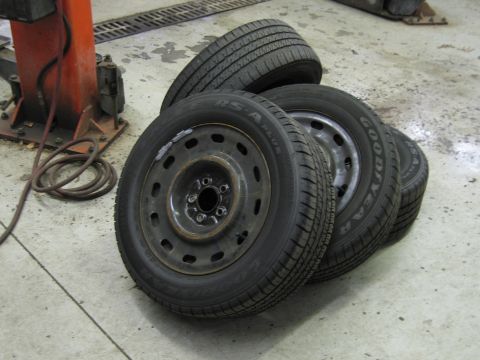 2001 Ford Crown Victoria - Stack of four tires and wheels on a concrete floor, possibly in a garage or workshop.