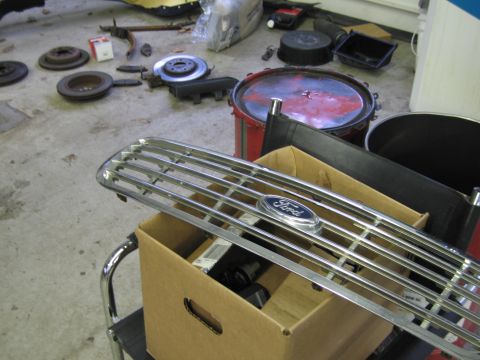 2001 Ford Crown Victoria - Various automotive parts, including a Ford grille, are laid out on a garage floor.