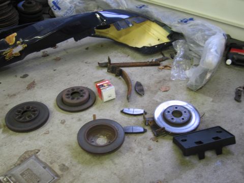 2001 Ford Crown Victoria - Various car parts, including brake rotors, pads, and a bumper, are laid out on a concrete surface.
