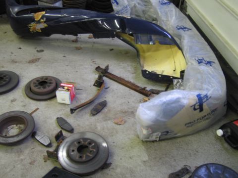 2001 Ford Crown Victoria - Various automotive parts, including a bumper and brake components, are laid out on a concrete floor.