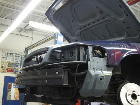 2001 Ford Crown Victoria - The front end of a vehicle is disassembled while elevated on a lift, with the hood open.