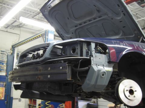2001 Ford Crown Victoria - The front end of a blue 2001 Ford Crown Victoria is disassembled while on a lift in a garage.