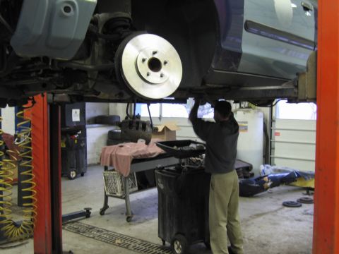 2001 Ford Crown Victoria - A mechanic works on the brake rotor of a vehicle elevated on a lift in a garage setting.
