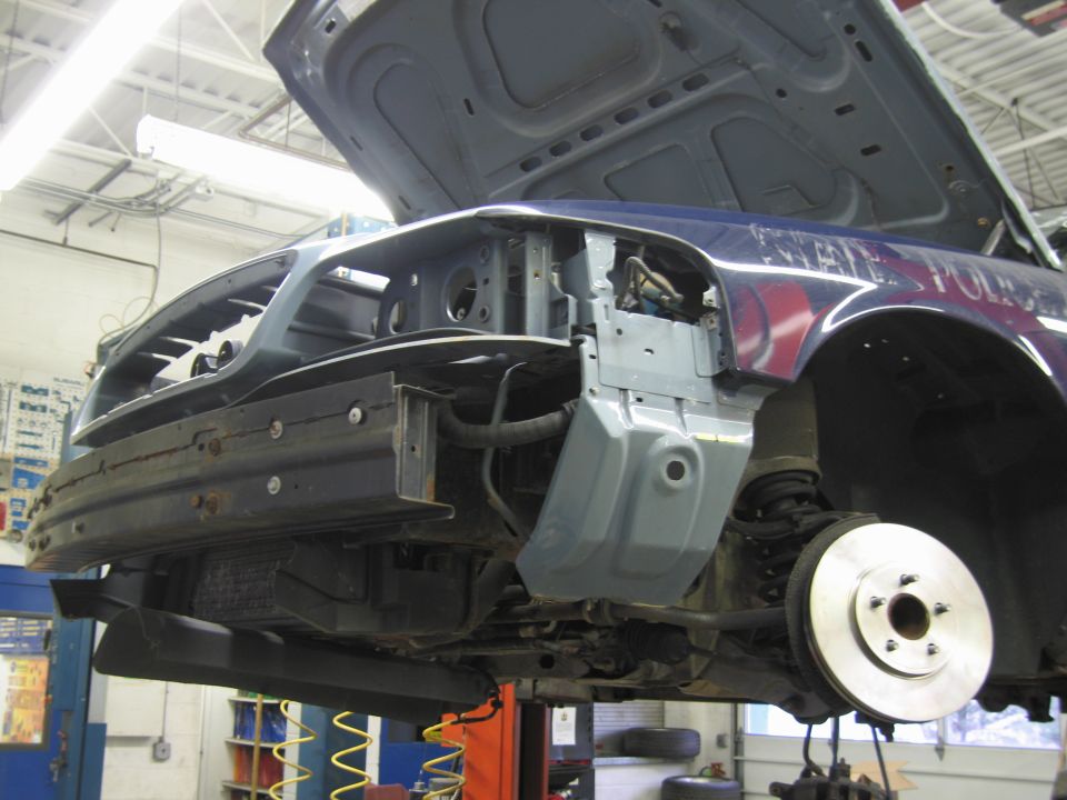 Front end of a 2001 Ford Crown Victoria disassembled, showing the engine bay and suspension components. The car has 'STATE POLICE' written on the fender