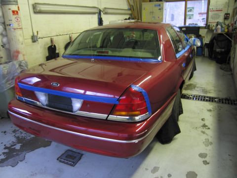 2001 Ford Crown Victoria - A red 2001 Ford Crown Victoria is parked in a garage, with blue tape applied to the rear for painting.