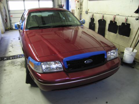 2001 Ford Crown Victoria - A red 2001 Ford Crown Victoria is parked in a garage, with blue tape applied to the front end for protection.