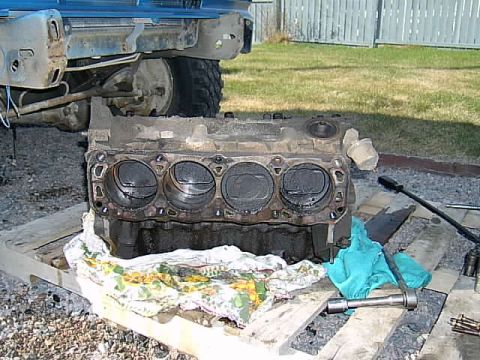 1983 Ford F-150 - A disassembled engine block rests on wooden pallets, with parts of a blue truck visible in the background.