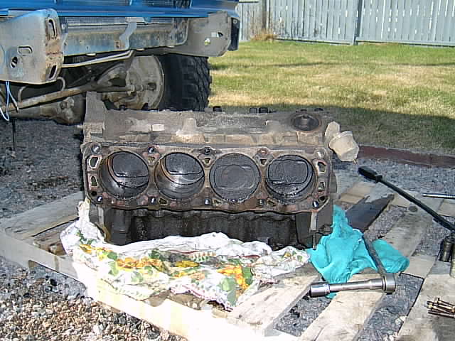 engine block sitting on wood pallets with tools nearby, truck frame visible above