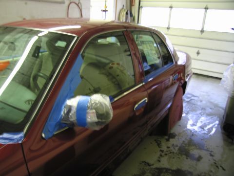 2001 Ford Crown Victoria - Side view of a red sedan with the driver's side door and mirror covered in blue tape and plastic, likely for protection during a repair or…