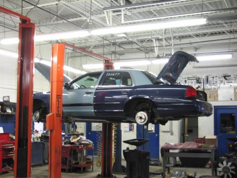 2001 Ford Crown Victoria - A two-tone blue sedan is elevated on a car lift in a garage, with its hood and trunk open.