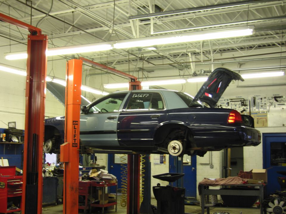 Side view of a two-tone blue and grey sedan on a car lift with hood and trunk open