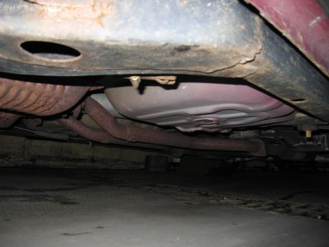 2001 Ford Crown Victoria - The underside of a red vehicle, revealing the exhaust system and fuel tank, with visible rust on the components.