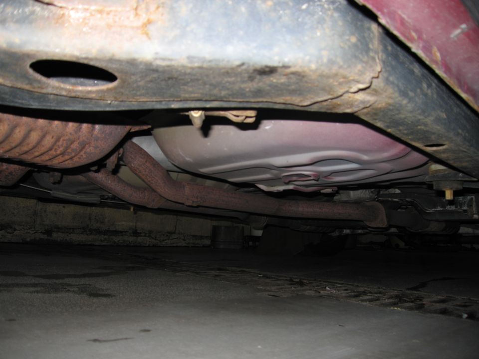 Underside of red vehicle showing exhaust pipes and fuel tank