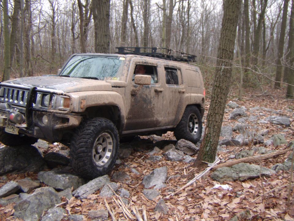 Mud-covered Hummer H3 driving over rocks in a forest, front-left view