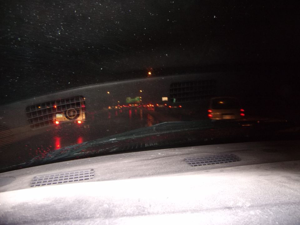 Interior view from a car at night, looking out at a wet highway with other vehicles