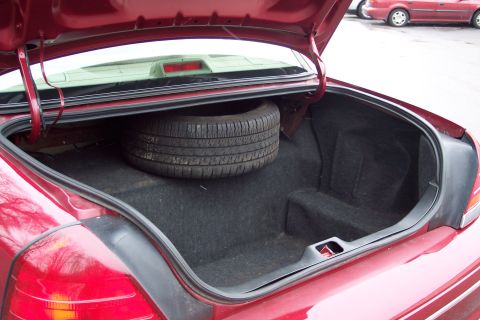 2001 Ford Crown Victoria - The trunk of a red 2001 Ford Crown Victoria is open, revealing a spare tire and its carpeted storage area.