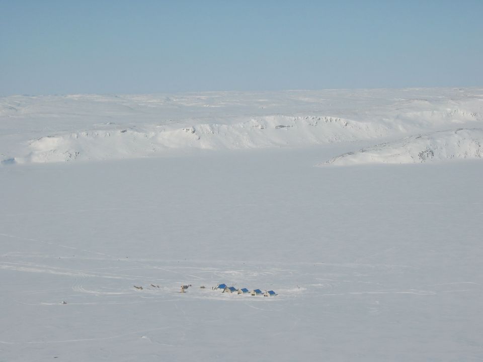 Distant blue tents and figures on a vast snow-covered Arctic landscape