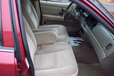 2001 Ford Crown Victoria - The interior of a 2001 Ford Crown Victoria features tan cloth seats, a center console with armrest, and a dashboard with a radio.
