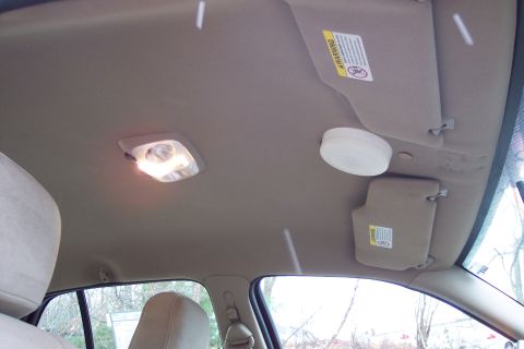 2001 Ford Crown Victoria - The interior ceiling of a car shows a lit dome light and two sun visors, one with a warning label attached.