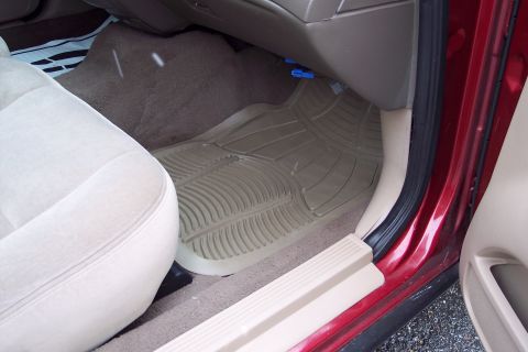 2001 Ford Crown Victoria - The interior of a car shows tan floor mats and a beige seat next to a red door frame.
