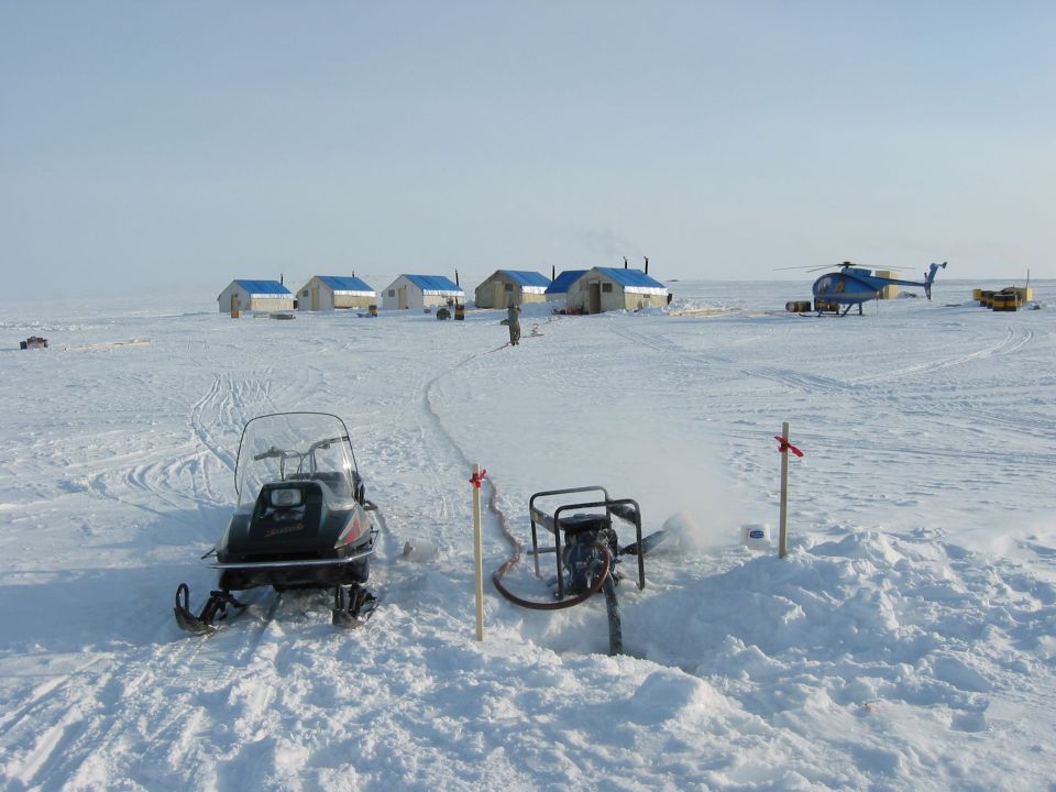 Snowmobile in foreground, helicopter and buildings in background on snowy plain