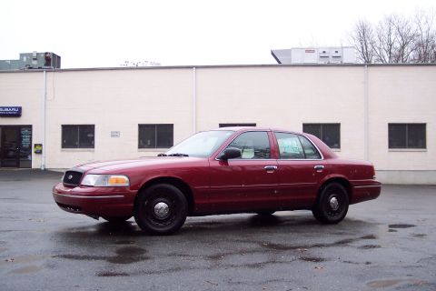 2001 Ford Crown Victoria - A red 2001 Ford Crown Victoria is parked on a wet asphalt lot in front of a light-colored commercial building.