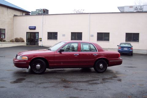 2001 Ford Crown Victoria - A red 2001 Ford Crown Victoria sedan is parked outside a building with another blue car in the background.