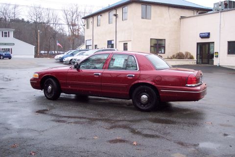 2001 Ford Crown Victoria - A red 2001 Ford Crown Victoria is seen from the side in a parking lot with other vehicles and a building in the background.