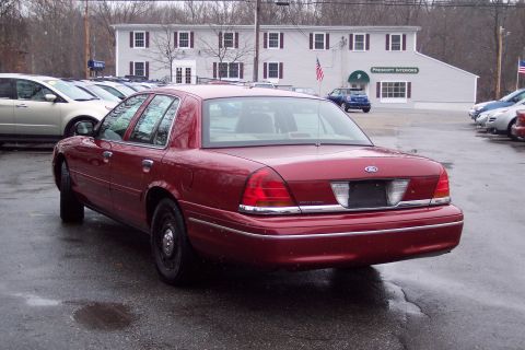 2001 Ford Crown Victoria - A red 2001 Ford Crown Victoria is seen from the rear quarter angle in a parking lot with other vehicles and a commercial building.