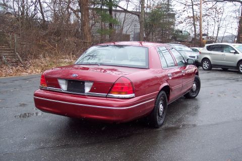 2001 Ford Crown Victoria - Rear view of a red 2001 Ford Crown Victoria sedan on a wet day. Another vehicle is parked nearby.