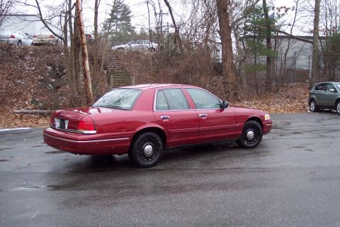 2001 Ford Crown Victoria - A red 2001 Ford Crown Victoria sedan is parked on a wet asphalt lot with trees and a building in the background.