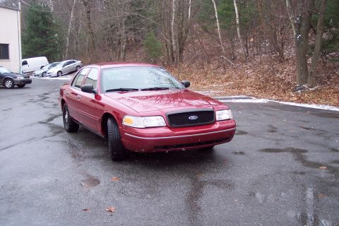 2001 Ford Crown Victoria - A red 2001 Ford Crown Victoria is parked outside on a wet, overcast day with trees in the background.