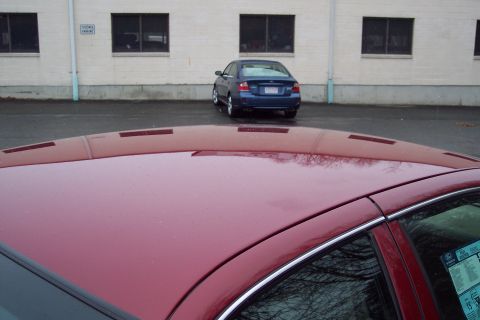 2001 Ford Crown Victoria - A red car's roof is in the foreground, with a blue sedan parked in the background.
