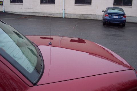2001 Ford Crown Victoria - The front portion of a red car is visible, including its hood and windshield, with a blue Subaru parked in the background.
