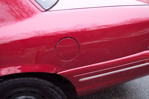 2001 Ford Crown Victoria - Rear quarter panel of a red 2001 Ford Crown Victoria, the gas cap door and chrome trim.