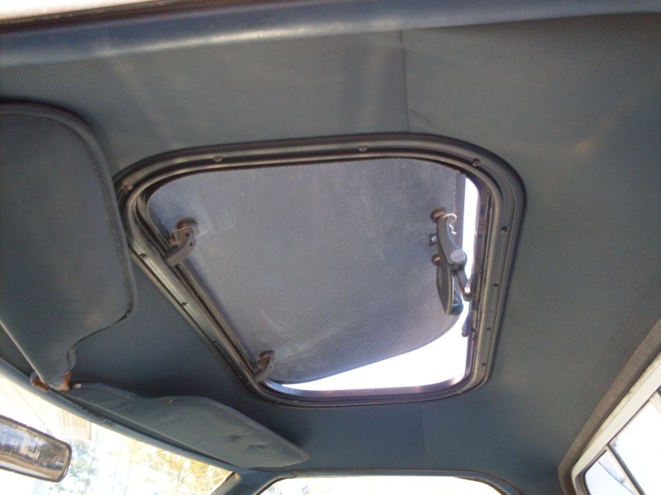 Open vent window/hatch in gray headliner with black latch, viewed from vehicle interior