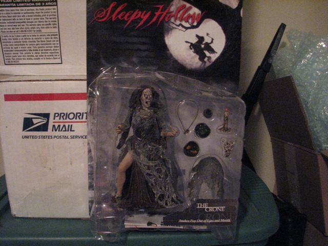 Action figure of The Crone from Sleepy Hollow in plastic packaging, next to Priority Mail boxes