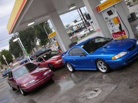 1998 Ford Crown Victoria - A blue 1998 Ford Mustang is parked at a gas station next to other vehicles.