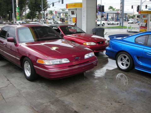 1998 Ford Crown Victoria - Three cars are at a gas station, with a maroon Ford Crown Victoria in the foreground.