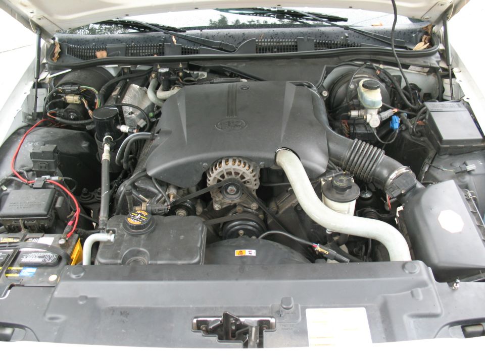 Engine bay of a white Ford sedan with black engine cover and visible accessory belt