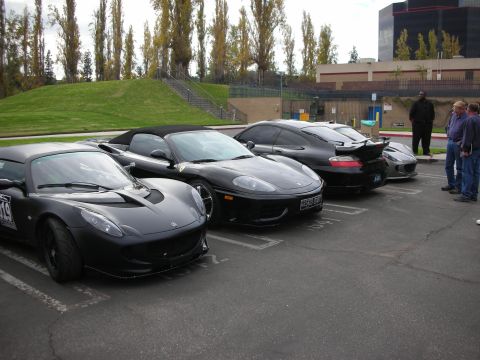 1998 Ford Crown Victoria - A line of black sports cars, including a Lotus Elise and a Ferrari, are parked in a lot.