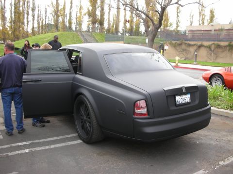 1998 Ford Crown Victoria - A matte black sedan with its door open, parked next to an orange sports car.