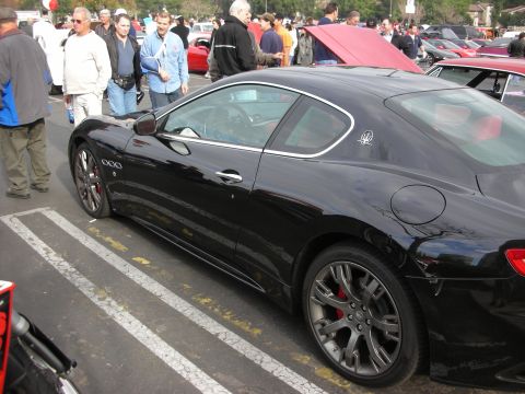 1998 Ford Crown Victoria - A black Maserati GranTurismo coupe is parked in a lot with other vehicles and people around.