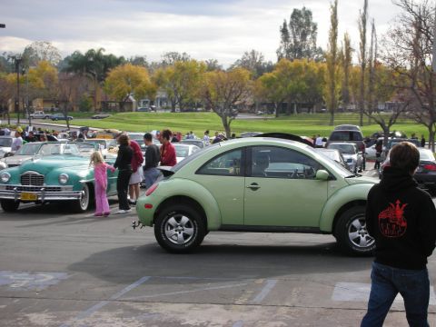 1998 Ford Crown Victoria - A light green Volkswagen Beetle is parked at an outdoor car show with other vehicles and people around.