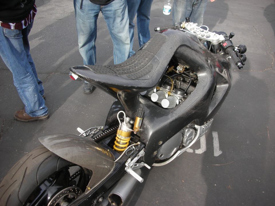Custom sport motorcycle with carbon fiber bodywork and exposed engine components. People stand around it