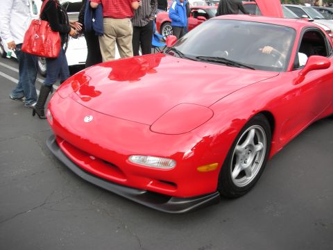 1998 Ford Crown Victoria - A bright red sports car is parked on asphalt, with several people standing nearby.