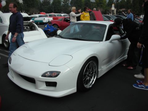 1998 Ford Crown Victoria - White sports car with custom wheels parked at an outdoor car show event.