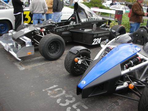 1998 Ford Crown Victoria - Two open-wheel race cars are parked side-by-side on asphalt, with spectators in the background.