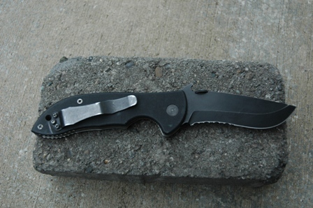 1991 Ford Bronco - A black folding knife with a partially serrated blade is placed on a gray brick.